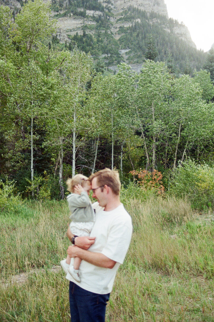 Danny Ellis, founder of AudioHaven, holding a young child in a meadow below the Wasatch mountains